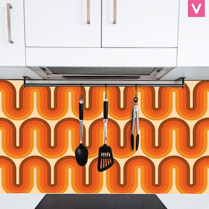 Op de afbeelding: Een keukenachterwand met een retro oranje en bruin golvend patroon. Een zwarte metalen stang met haken hangt boven de achterwand en houdt een zwarte spatel, een zwarte lepel en een zwarte tang vast.