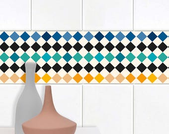 May include: A white tiled wall with a decorative border of black and white diamond shapes. The border features a gradient of blue, teal, and yellow colors. Two ceramic vases, one gray and one light brown, are placed on a white surface in front of the wall.