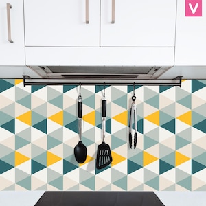 Puede incluir: Utensilios de cocina colgados debajo de armarios blancos. Una cuchara, espátula y pinzas negras cuelgan de una barra de metal. El protector contra salpicaduras presenta un patrón geométrico de triángulos turquesa, amarillos y grises.