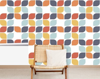 May include: A mid-century modern wallpaper roll with a repeating pattern of stylized leaf shapes in orange, yellow, blue, and gray on a white background. A wooden chair with a woven seat and a white pillow is in front of the wallpaper.