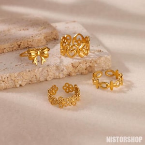 Peut inclure: Quatre bagues dorées avec des motifs complexes. Les bagues présentent un nœud, un cœur, un motif floral et un motif géométrique.