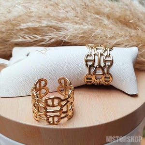 Peut inclure: Deux bagues en or avec un design de chaîne entrelacée. Les bagues sont sur un présentoir blanc.