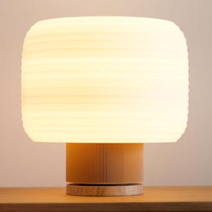 May include: A contemporary table lamp featuring a cylindrical base and a rectangular lampshade. The lampshade is a soft white, and the base is light brown. The lamp is on a wooden table, with measurements in cm.