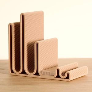 May include: A beige, 3D-printed desk organizer with a unique, curved design. The organizer has multiple sections for holding items like pens, phones, or small notebooks. The textured surface adds visual interest to this modern office accessory.