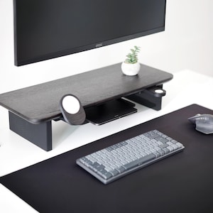 May include: A dark wood-tone desk riser with a small plant in a white pot. A black keyboard, mouse, and mousepad are on the desk. A black monitor is mounted above the desk riser.