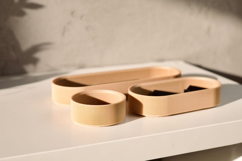 May include: Three beige ceramic trays with a ribbed texture. The trays are oval shaped and are nested inside each other.