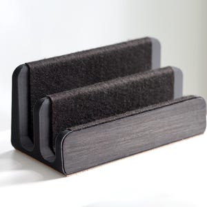Puede incluir: Un organizador de escritorio de tres niveles con un diseño moderno. El organizador presenta un material gris oscuro, similar al fieltro, para las secciones superiores y un acabado de vetas de madera oscura en la base. Diseñado para guardar papeles y suministros de oficina.