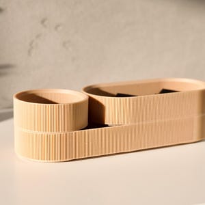 May include: A set of three beige, cylindrical containers with a ribbed texture. The containers are stacked on top of each other, with the largest container at the bottom and the smallest container at the top.