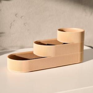 May include: Three beige oval-shaped containers stacked on top of each other. The containers have a ribbed texture and are made of a lightweight material.