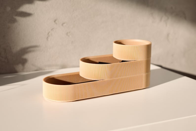May include: Three beige oval-shaped containers stacked on top of each other. The containers have a ribbed texture and are made of a lightweight material.