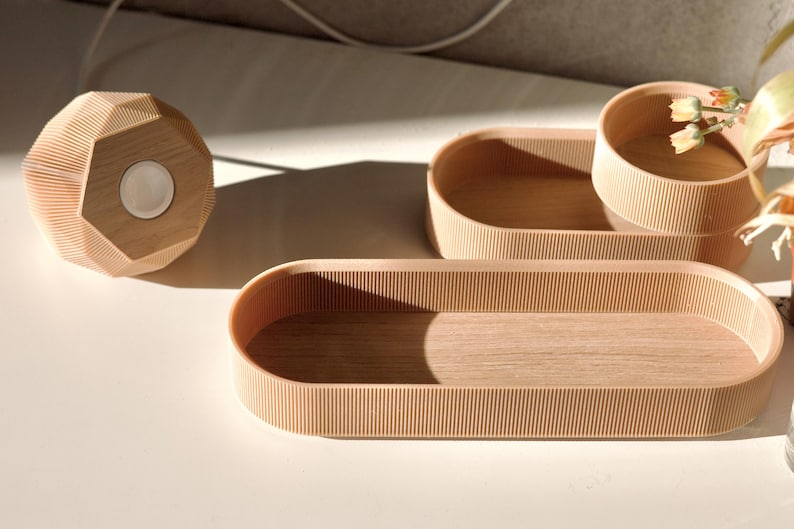 May include: Three wooden trays with a ribbed texture. The trays are oval shaped and made of light brown wood. The largest tray is in the foreground, and the smallest tray is in the background.
