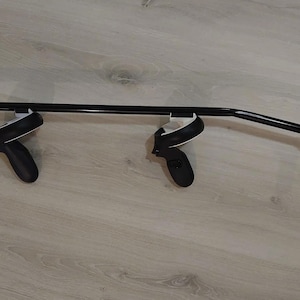 May include: A black metal stand with two black VR controllers attached. The stand is mounted on a wall.
