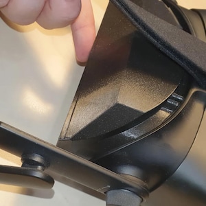 以下が含まれることがあります： 調整可能なストラップとパッド入りのイヤーカップを備えた黒いVRヘッドセット。ヘッドセットは、マット仕上げの洗練されたモダンなデザインです。画像は、ヘッドセットの側面をクローズアップで示しています。