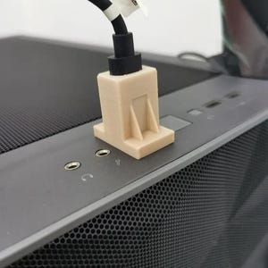 Könnte beinhalten: Eine beige 3D-gedruckte Komponente mit einem schwarzen Kabel, die auf einem dunkelgrauen Computergehäuse liegt. Die Komponente hat eine rechteckige Basis und eine vertikale Stützstruktur. Das Gehäuse hat eine perforierte Frontplatte.