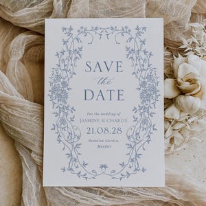Peut inclure: Carte Save the Date blanche avec un motif floral bleu. Le texte indique « SAVE the DATE » avec les détails du mariage de Jasmine & Charlie, la date du 21.08.28 et Beaulieu Garden, Mayfair.
