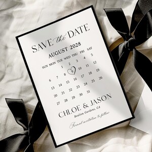 Op de afbeelding: Een zwart omkaderde save-the-date kaart met een kalender voor augustus 2028. De kaart toont de namen Chloe & Jason en is vastgebonden met een zwart lint. De trouwdatum is gemarkeerd met een hart.