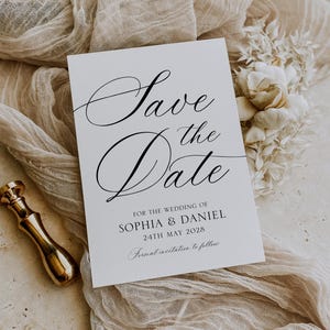 May include: A white wedding invitation card with the text "Save the Date" in elegant black script. The card includes the names Sophia & Daniel and the date May 24th, 2028. A gold wax seal and decorative fabric are in the background.