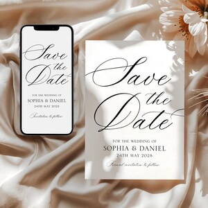 Puede incluir: Una invitación de boda y un teléfono inteligente que muestra el mismo diseño. El texto en ambos dice "Save the Date" en una escritura elegante, seguido de los nombres Sophia & Daniel y la fecha 24 de mayo de 2028. El fondo es una tela suave y neutra.