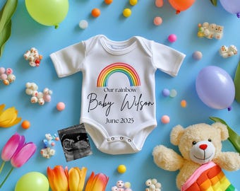 Può includere: Un body bianco con un arcobaleno e il testo "Our rainbow Baby Wilson June 2025". Il body è circondato da palloncini colorati, tulipani e un orsacchiotto avvolto in una coperta arcobaleno.