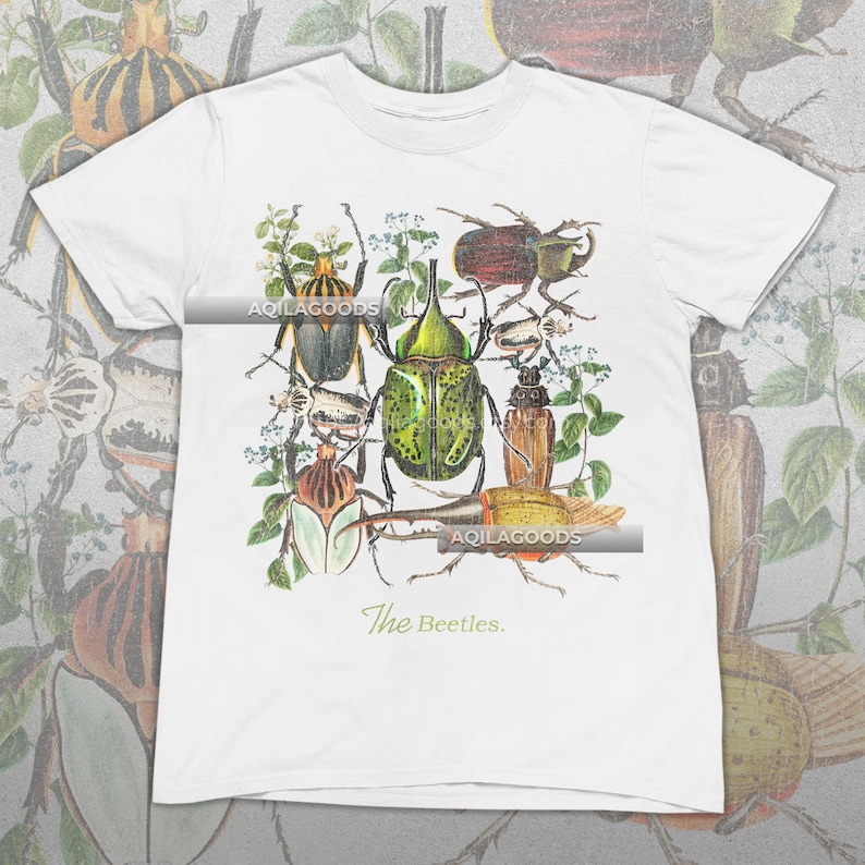 May include: White t-shirt featuring a detailed illustration of various beetles in shades of green, brown, and yellow, with floral accents. The text "The Beetles" is printed in a script font at the bottom. The brand name "AQILAGOODS" is printed on the shirt.