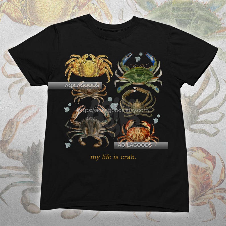 May include: Black t-shirt featuring a watercolor illustration of six different crabs in shades of gold, green, brown, and red. The text "my life is crab" is printed at the bottom. The brand name "AQILAGOODS" is printed on the shirt.