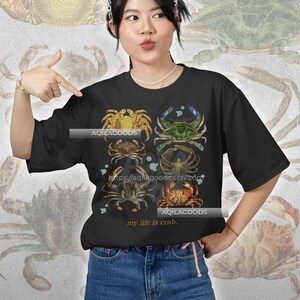 May include: Black t-shirt featuring a collage of crab illustrations in various colors. The shirt includes the text "my life is crab" and the shop's URL. The crabs are depicted in shades of yellow, green, brown, and red, creating a vintage aesthetic.