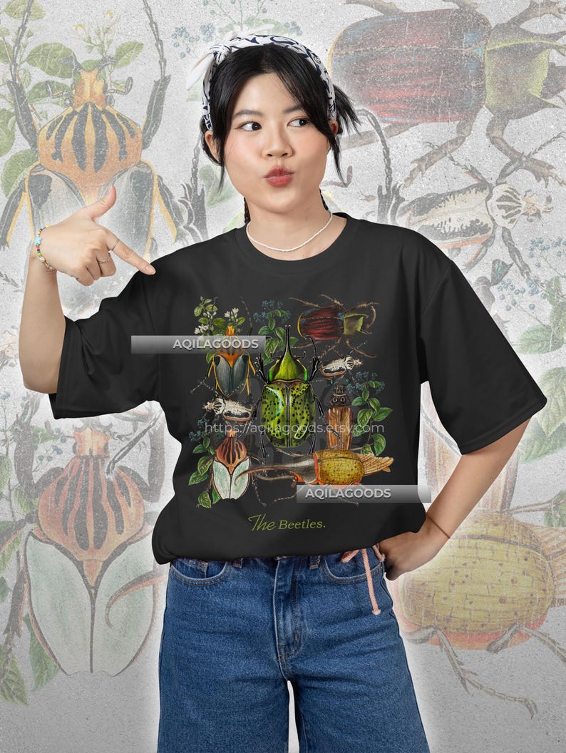 May include: Black t-shirt featuring a detailed illustration of various beetles in shades of green, brown, and white, with botanical elements. The text "The Beetles" is printed below the graphic. The Etsy shop URL is also visible.