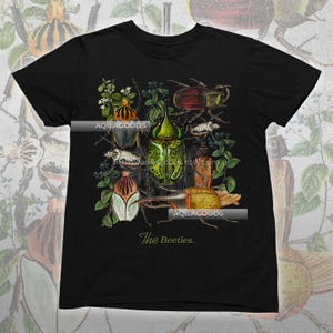 May include: Black t-shirt featuring a detailed illustration of various beetles in shades of green, brown, and red, surrounded by foliage. The text "The Beetles" is printed in a cursive font at the bottom.