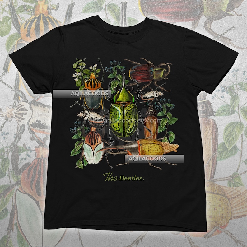 May include: Black t-shirt featuring a detailed illustration of various beetles in shades of green, brown, and red, surrounded by foliage. The text "The Beetles" is printed in a cursive font at the bottom.