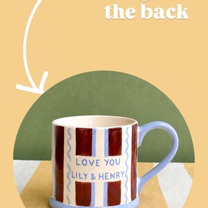 May include: A ceramic mug with a blue handle and base, featuring a design of alternating maroon and white vertical stripes. The mug has the text "LOVE YOU LILY & HENRY" in blue.