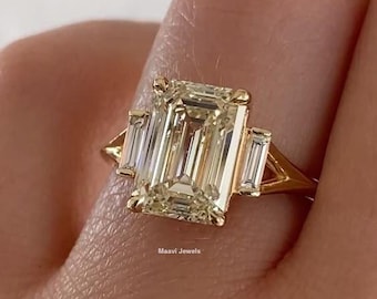 May include: A gold ring featuring a large, rectangular, light yellow gemstone with two smaller rectangular stones on either side. The ring has a classic, elegant design. The text "Maavi Jewels" is visible.