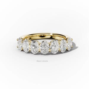 May include: A gold ring with seven oval-cut diamonds. The diamonds are set in a row, creating a continuous sparkle. The ring is displayed on a white background, emphasizing the brilliance of the gemstones. The ring is a piece of jewelry.