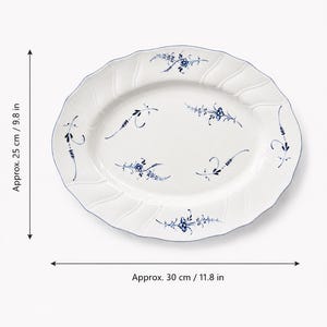 Può includere: Un piatto da portata ovale in ceramica bianca con bordo smerlato e motivi a rametti floreali blu. Il piatto misura circa 25 cm di larghezza e 30 cm di lunghezza, come indicato dalle linee di misurazione presenti nell'immagine.