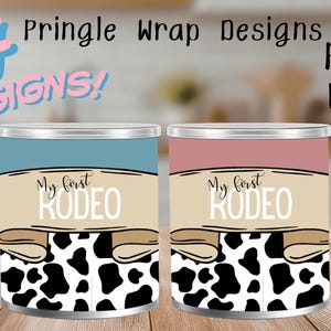 May include: Two Pringle can wraps with the text "My first RODEO". One can has a blue top, the other a pink top. Both have a tan banner with the text and a black and white cow print design.