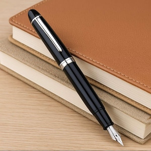 May include: A black fountain pen with a silver trim and a fine nib, resting on top of two notebooks.