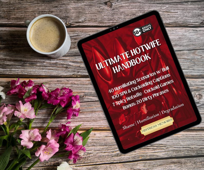 May include: A digital tablet displaying the text "ULTIMATE HOTWIFE HANDBOOK" with additional text about scenarios, captions, and games. A cup of coffee and a bouquet of pink and purple flowers are also on the wooden surface.