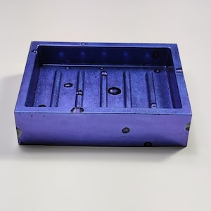 Puede incluir: Un jabonera de color morado con una superficie texturizada y un diseño elevado con nervaduras. La jabonera tiene forma rectangular y está hecha de un material duradero.