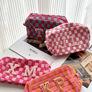 Pode incluir: Quatro nécessaires coloridas com letras iniciais. As bolsas apresentam um padrão xadrez em rosa, laranja e verde. As letras são adornadas com pérolas. As bolsas estão em cima de uma revista.