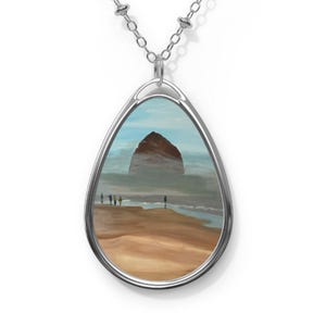 Peut inclure: Collier argenté avec un pendentif en forme de goutte d'eau représentant une peinture de paysage. La peinture montre une scène de plage avec une grande formation rocheuse, un ciel bleu et des personnages sur le rivage. Le pendentif mesure environ 3,8 cm de long.