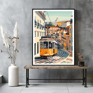 Può includere: Una stampa artistica incorniciata raffigurante un tram giallo che viaggia sui binari lungo una strada stretta di Lisbona, in Portogallo. L'illustrazione mostra edifici colorati, linee elettriche aeree e il testo LISBON Portugal in lettere bianche.