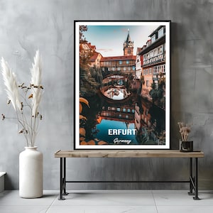 May include: Framed print featuring a scenic view of Erfurt, Germany, with a canal reflecting the architecture. The image showcases buildings with red-tiled roofs, a church tower, and the text "ERFURT Germany" in white.