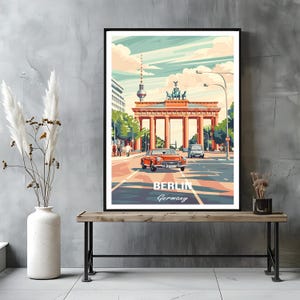 May include: A framed travel poster print featuring the Brandenburg Gate and the Berlin TV Tower in the background. An orange vintage car drives on a city street in the foreground. The text BERLIN Germany is printed at the bottom of the artwork.