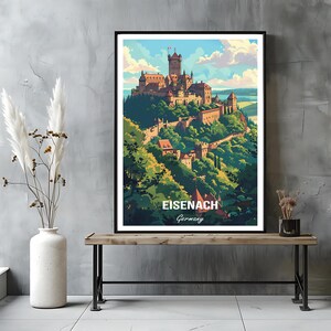 May include: A framed art print featuring a stylized illustration of the Wartburg Castle in Eisenach, Germany. The artwork depicts the castle atop a green hill, with the text "Eisenach Germany" at the bottom. The print is displayed on a wooden bench.