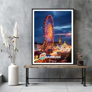 Könnte beinhalten: Ein gerahmter Druck einer nächtlichen Jahrmarktszene in Hamburg, Deutschland. Ein hell beleuchtetes Riesenrad dominiert das Bild, mit anderen beleuchteten Fahrgeschäften und Gebäuden im Hintergrund. Der Text "HAMBURG Germany" ist unten zu sehen.
