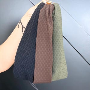 May include: Three headbands in black, brown, and olive green, each with a textured, checkered pattern. The headbands are held together by a gold-coloured clasp.