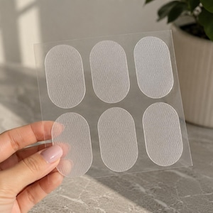 May include: A clear plastic sheet featuring five oval-shaped adhesive patches with a textured, matte surface. The patches are arranged in two rows, with three in the top row and two in the bottom row, designed for application as protective stickers.