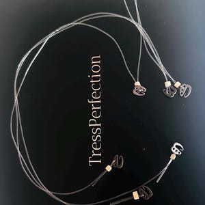 May include: Transparent hair extensions with small metal clips, set against a black backdrop, with the text "TressPerfection". The extensions are arranged in a circular pattern, with several clips visible.