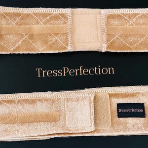 May include: Two beige hair bands with a diamond pattern and a soft, velvety texture are displayed. The text "TressPerfection" is printed in gold. One band has a Velcro closure and a small black label with the brand name.