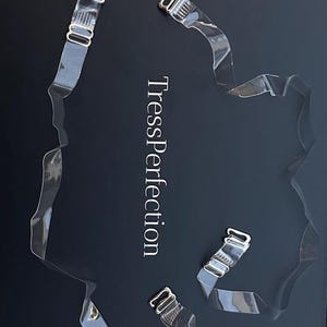 May include: Transparent bra straps with metal clasps are shown against a dark backdrop. The text "TressPerfection" is printed in silver. The straps are clear and appear to be made of plastic or a similar material.