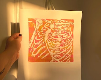 Könnte beinhalten: Ein abstrakter Druck in Orange- und Gelbtönen. Das Kunstwerk zeigt ein stilisiertes Design mit organischen Formen und Linien. Der Druck wird auf weißem Papier angezeigt und von einer Hand gehalten.